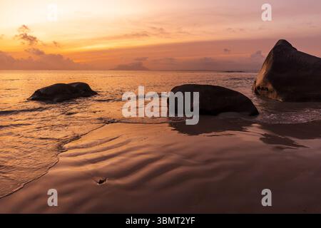 Küstenlandschaft der Insel Mahe, Seychellen. Eine malerische Strandszene mit glatten Felsen und ruhigem Wasser, beleuchtet von einem lebhaften Sonnenuntergang. Die Mischung Stockfoto