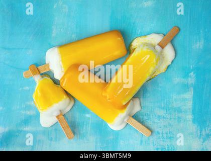 Ein schmelzendes Eis mit einem Holzstab, der eine leuchtende gelbe Farbe auf blauem Hintergrund zeigt, sorgt für einen süßen Leckerbissen Stockfoto