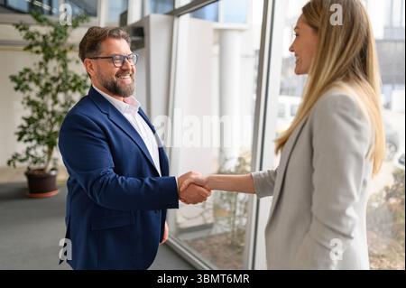 Lächelnder Geschäftsmann mit Brille, der nach einem erfolgreichen Geschäftsabschluss im Tagungsraum die Hand schüttelt Stockfoto