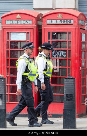 Männliche und weibliche Metropolitan Police Polizisten auf dem Schlag an zwei roten Telefonzellen in Whitehall, Westminster, London, Großbritannien Stockfoto