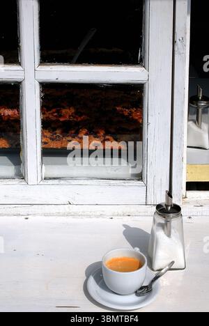 Stillleben mit einer Tasse Kaffee und einem Zuckerspender auf einer weißen Fensterbank in der Sonne. Stockfoto