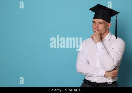 Nachdenklicher Schüler nach Abschluss auf hellblauem Hintergrund. Leerzeichen für Text Stockfoto