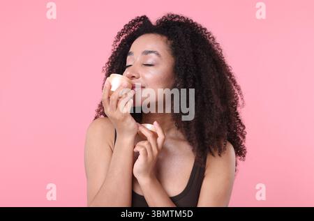 Schöne brasilianische Frau mit einem Glas Kollagencreme auf rosa Hintergrund Stockfoto