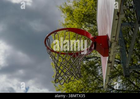 Nahaufnahme eines Basketballkörpers, zentriert im Rahmen. Der rote Rand des Rings und die orange lackierte Rückwand sind sichtbar, während das Netz in der Sonne leuchtet Stockfoto