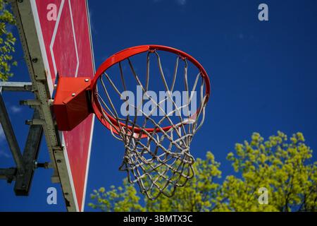 Nahaufnahme eines Basketballkörpers, zentriert im Rahmen. Der rote Rand des Rings und die orange lackierte Rückwand sind sichtbar, während das Netz in der Sonne leuchtet Stockfoto