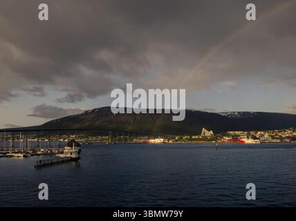 Regenbogen über die Tromsø-Brücke und die Arktische Kathedrale in der norwegischen Küste, mit dramatischen Wolken und arktischen Bergen dahinter. Stockfoto