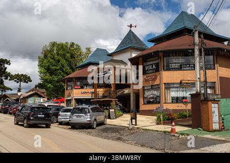 Geschäftskomplex im alpinen Stil mit Folk Fabrica, Cafeteria und Geschäften auf der Monte Verde Avenue, mit geparkten Autos unter bewölktem Himmel. Stockfoto