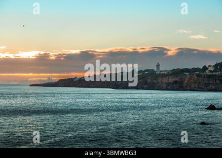 Santa Marta Lighthouse in Cascais, Portugal, bei Sonnenuntergang. Das berühmte Wahrzeichen an den Klippen ist in den warmen Glanz der Sonne über der Küste getaucht Stockfoto