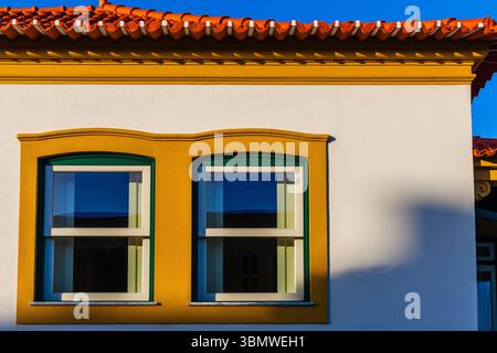 Ein leuchtend gelb-grüner Fensterrahmen mit zwei modernen Fenstern steht vor einer stark weißen Wand und zeigt ein markantes architektonisches Detail Stockfoto