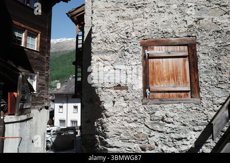 Alte Steinfassade mit verwitterter Holztür und kleinem Fenster in Zermatt, Schweiz Stockfoto