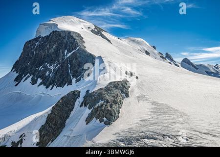 Ein atemberaubender Blick auf einen schneebedeckten Berggipfel mit Kletterern, die an klaren Tagen zum Gipfel hinaufsteigen. Stockfoto