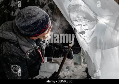 Fairbanks, USA - 21. Februar 2023: Nahaufnahme eines Künstlers mit Meißel, der nachts an Eisskulpturen arbeitet, für Eiskunstweltmeisterschaften, Eisskulpturwettbewerb und -Festival Stockfoto