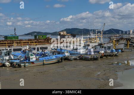 Seosan, Südkorea. September 2020:. Fischerboote stecken bei Ebbe im Hafen von Seosan unter wolkenblauem Himmel auf Gezeiten fest Stockfoto