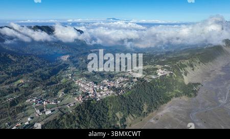 Ein Blick aus der Vogelperspektive auf Cemoro Lawang zeigt ein Flickenteppich von Feldern und Häusern am Rande der riesigen vulkanischen Ebene mit nebeligen Bergen Stockfoto