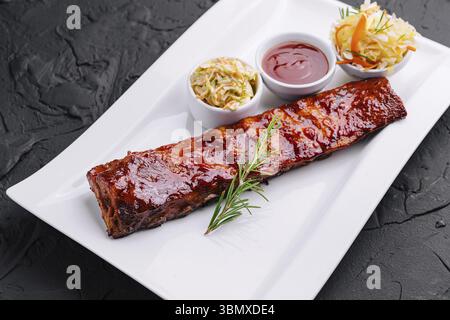 Stillleben, gegrillte Schweinerippchen in Grillsoße und Honig mit Sauerkraut auf weißem Teller Stockfoto