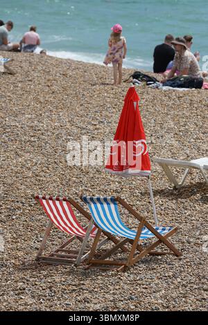 Farbenfrohe Deck Stühle und Regenschirm an einem entspannenden Kieselstrand. Brighton, England Stockfoto