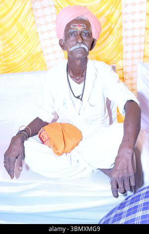 Älterer indischer Mann in traditioneller Kleidung mit Turban und Stirn tilak, der drinnen sitzt Stockfoto
