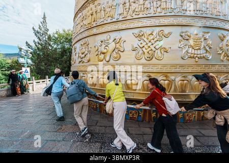 Shangri-La, China - 21. Oktober 2024: Aus einem niedrigen Winkel sehen Touristen und Pilger in farbenfroher traditioneller Kleidung das riesige goldene Gebetsrad in SH Stockfoto
