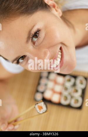 Hochwinkelansicht einer Frau, die Sushi zwischen Essstäbchen hält Stockfoto