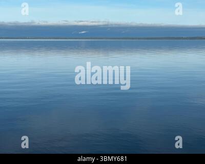 Der ruhige Ozean erstreckt sich zum Horizont hin und reflektiert den blauen Himmel und die weichen Wolken darüber. Stockfoto