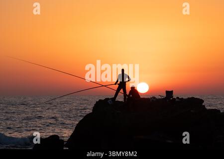Fischer fischen abends am Meer an der Mittelmeerküste von Cäsarea in Israel bei Sonnenuntergang in Richtung der untergehenden Sonne. Hochwertige Fotos Stockfoto