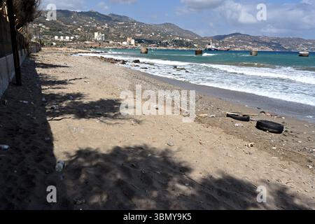 Verschiedene Arten von Müll, einschließlich Reifen, Plastikflaschen und andere gefährliche Abfälle, sind am Strand in der Nähe des Ankerbereichs für Frachtschiffe verstreut. Stockfoto