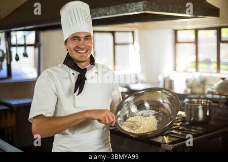 Koch, der Teig in einer Edelstahlschale auf der Arbeitsplatte in der professionellen Küche mit Sonnenlicht verrührt Stockfoto