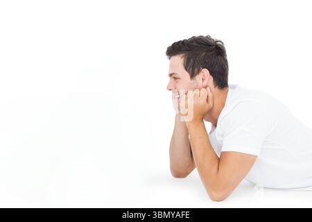Mann, der auf glatter weißer Studiooberfläche auf Ellbogen nach links in minimalistischem Porträt liegt, Kopierraum Stockfoto