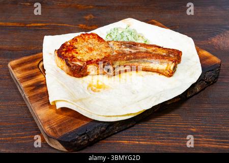 Saftige Schweinerippchen ruhen auf einem warmen Fladenbrot, garniert mit knusprigem Krautsalat. Das Gericht wird auf einem rustikalen Schneidebrett aus Holz präsentiert und bietet Delikatessen Stockfoto