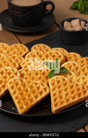 Köstliche Waffeln in Herzform, serviert mit Kaffee und Zucker auf einem Holztisch Stockfoto