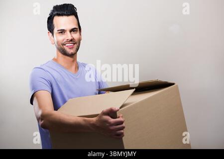 Mann, der einen großen, oben offenen Karton hält, während er im Raum mit einer hellen neutralen Wand steht Stockfoto