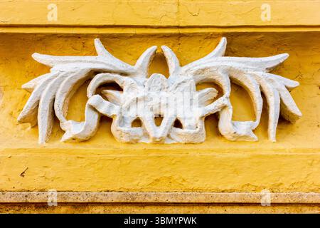 Kunstvolles weißes dekoratives Relief auf gelber Wand in Nahaufnahme Stockfoto