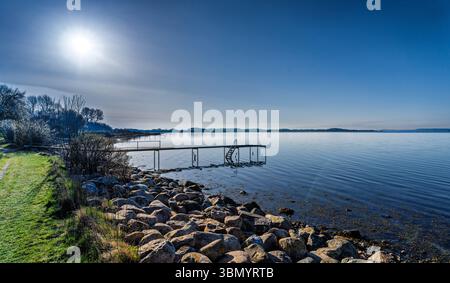Eine friedliche Küstenszene mit einem Pier, der sich in ruhiges Wasser erstreckt, umgeben von ruhiger Natur und klarem blauem Himmel, die ein Gefühl der Ruhe und des Friedens weckt Stockfoto