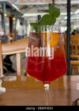 Ein Glas Aperol Spritz Cocktail, dekoriert mit einem Stück Orange und einem Zweig Minze auf einem Restauranttisch Stockfoto