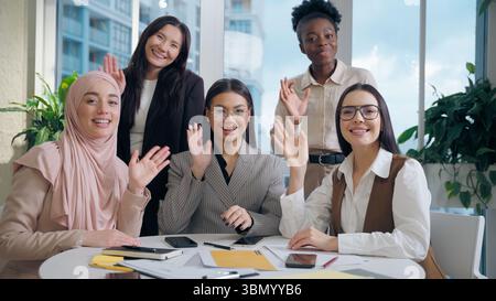 Glückliche fröhliche multiethnische vielfältige Geschäftsfrauen weibliche Geschäftsfrauen Teamkollegen multirassische Gruppe Blick auf kamerasfreundliche winkende Hände Stockfoto