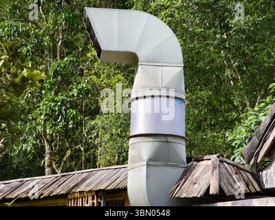 Eine gekrümmte industrielle Abluftdüse aus Metall, die auf dem Dach eines Gebäudes mit einer Bambusstruktur befestigt ist Stockfoto