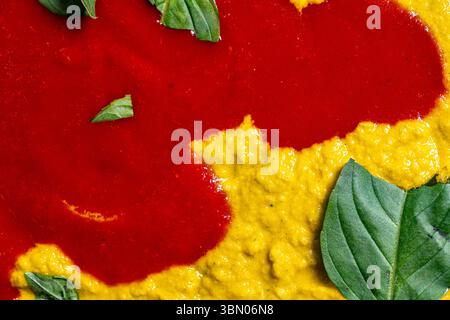 Hintergrund mit gelber und roter Soße mit Basilikumblättern. Soße für Pasta oder Pizza zubereiten. Italienische Küche. Hochwertige Fotos Stockfoto