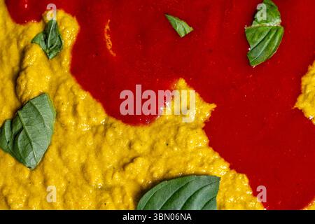 Hintergrund mit gelber und roter Soße mit Basilikumblättern. Soße für Pasta oder Pizza zubereiten. Italienische Küche. Hochwertige Fotos Stockfoto