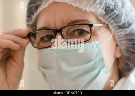 Eine erfahrene Ärztin mit medizinischer Maske starrt direkt in die Kamera. Der Moment erfasst Entschlossenheit, Pflege und medizinische Verantwortung in einem Krankenhaus. Stockfoto