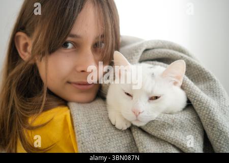 Eine heranwachsende Frau, die ihre unberührte weiße Katze in liebevoller Umarmung hält. Schöne Demonstration von Tierfreundschaft und Hingabe. Stockfoto