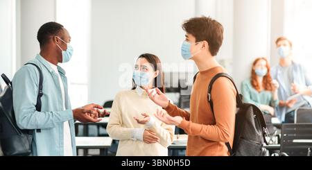 Lächelnde internationale Studenten tragen medizinische Masken und reden Stockfoto