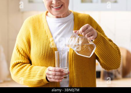 Nahaufnahme einer nicht erkennbaren Großmutter, die Wasser in das Glas gießt Stockfoto