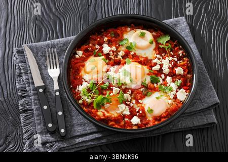Shakshuka, reichhaltige Tomatensauce mit Eiern in einer Auflaufform pochiert, bestreut mit zerbröckeltem Fetakäse und Koriander, horizontaler Blick von Stockfoto