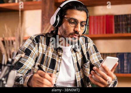 Indian Male Student Mit Smartphone Learning Sitzen In Der Bibliothek Stockfoto
