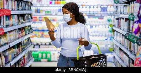 Junge schwarze Frau in Gesichtsmaske Einkaufen für Lebensmittel bei Riesiger Supermarkt während der covid-19 Sperre Stockfoto