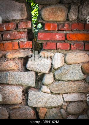 Eine Nahaufnahme zeigt eine verwitterte Wand aus Steinen und Ziegeln, die ihre einzigartigen Texturen und Farben zeigt. Stockfoto