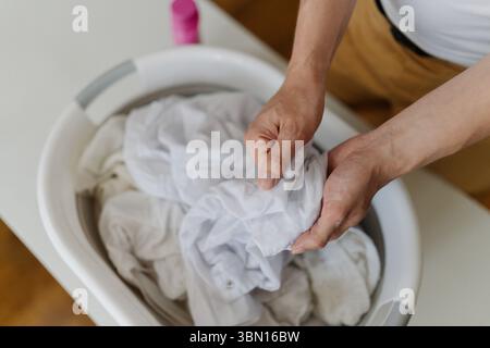 Draufsicht eines nicht erkennbaren Mannes, der weiße Kleidung zum Waschen vorbereitet und mit Fleckenentferner in das Becken getaucht, bevor er sie in die Waschmaschine für stellt Stockfoto