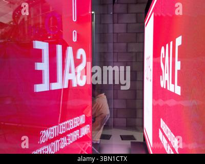 Ein großer LED-Bildschirm mit einem auffälligen rot-rosa Verkaufsschild beleuchtet ein Londoner Ladenfenster, während ein Käufer von hinten vorbeikommt. UK Stockfoto