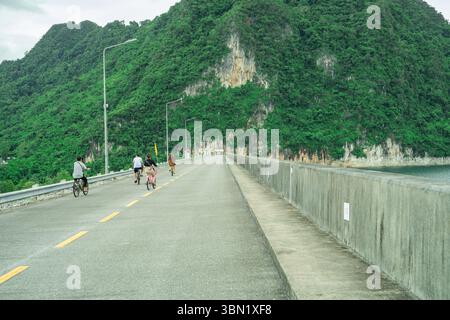 Die Familie radelt am Nachmittag gemeinsam auf einer Betonstraße auf einem malerischen Damm, der von Kalksteinklippen umgeben ist, und fördert so den umweltfreundlichen Tourismus Stockfoto