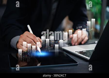 Geschäftsmann analysiert Finanzdaten und Wachstumstrends auf einem Tablet mit digitalen Diagrammen und Diagrammen und arbeitet an einem Notebook in einem modernen Büro. Stockfoto